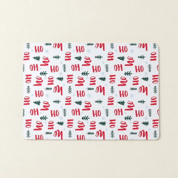 Rechthoekige Placemat Kerst HoHoHo met een wit oppervlak, versierd met rode kerstteksten, groene dennenboompjes en kleine lichtblauwe sneeuwvlokken.