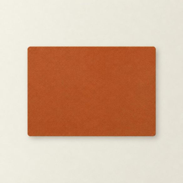Een rechthoekige placemat van oranje kunstleer met een subtiele textuur, plat neergelegd op een lichte ondergrond voor een strakke presentatie.