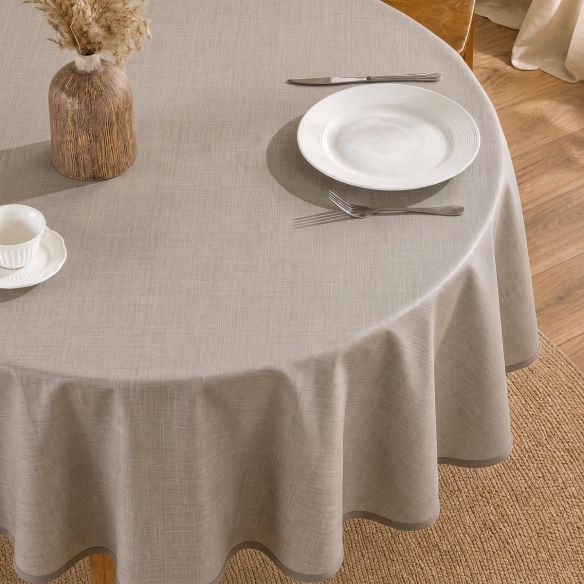 Rond beige tafelzeil met een subtiele linnenstructuur, gedrapeerd over een ronde tafel met een wit bord, bestek en een decoratieve vaas erop.