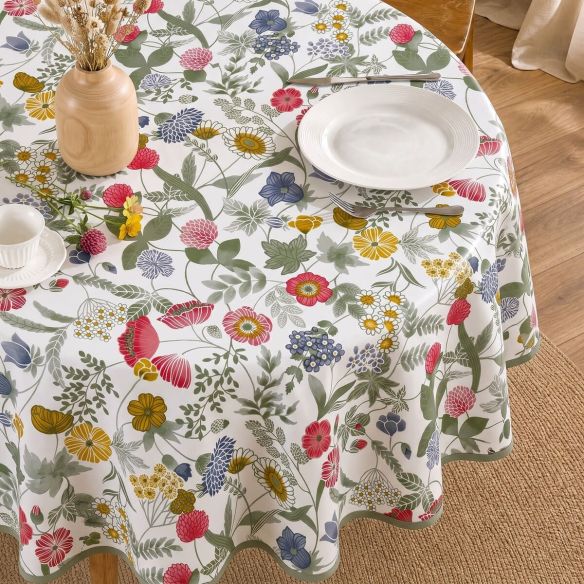 Rond tafelzeil Hilda met een kleurrijk bloemenpatroon op een witte ondergrond, gedekt met servies op een houten tafel in een lichte kamer.