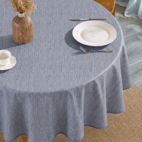 Rond tafelzeil Namaste Denim in blauw met verticaal streeppatroon, gedekt op een tafel met een bord, bestek, kopje en een decoratieve vaas.