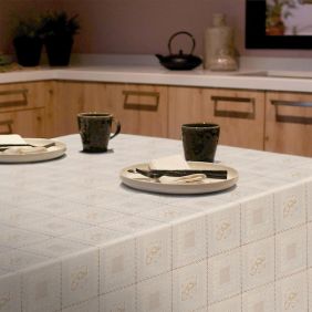 Lichtblauw tafelzeil met een wit kantpatroon in vierkante vakken, gedekt op een tafel met borden, servetten en donkere mokken in een keuken.