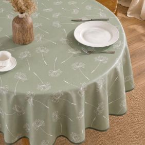 Rond groen tafelzeil met wit paardenbloemmotief, gedekt met een wit bord, bestek en een vaas op een houten tafel in een sfeervolle setting.