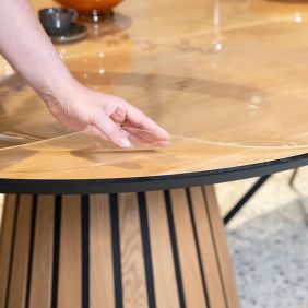 Hand die een rond, doorzichtig tafelzeil van 2mm dik optilt van een houten tafelblad voor bescherming van het oppervlak.